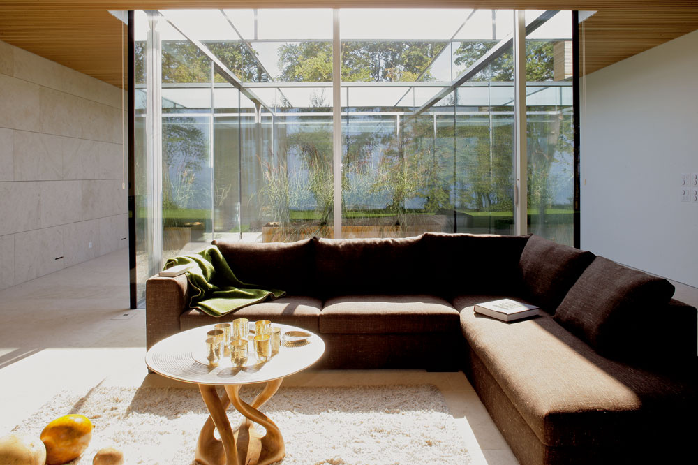 V obývačke si môžete transparentnosť domu užiť naplno – na jednej strane sklenená severná fasáda s výhľadom, na druhej sklené steny slnečného átria. (Sedačka značky Flexform, stôl a koberec od spoločnosti Redbox, za stenou s kozubom je otvorená spálňa.)