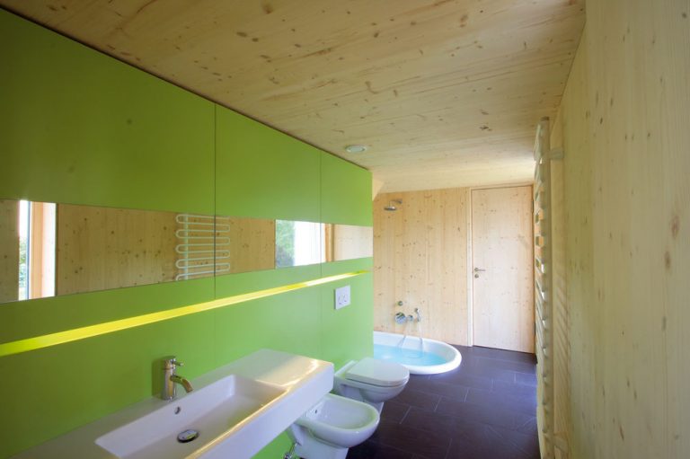 Kúpeľňa je prístupná veľmi prakticky – ako zo vstupného priestoru, tak aj z kuchyne, nie je však priechodná. Každodenná komunikácia je vyriešená okolo nej, popri sklenenej záhradnej fasáde.
