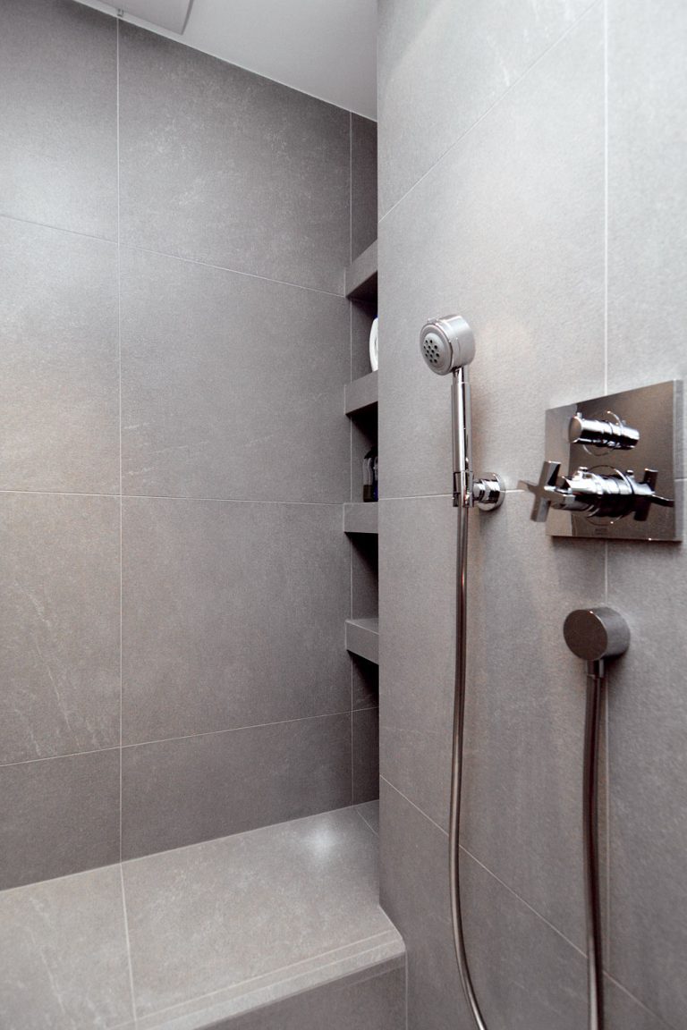 Úložné priestory na predmety každodennej potreby býva ťažké navrhnúť tak, aby boli poruke a zároveň neviditeľné. V kúpeľni to architekt dosiahol zapustením políc za úroveň steny tak, aby boli pri vstupe do kúpeľne neviditeľné, ale pri používaní sprchy ľahko dosiahnuteľné.
