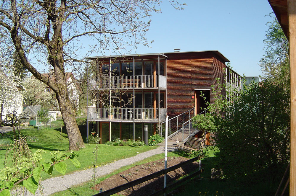 Trojpodlažný bytový dom v rakúskom Voralbergu je tiež postavený v pasívnom štandarde. Pre tento spôsob výstavby je typický kompaktný tvar s južne situovanými zasklenými fasádami. Ďalším charakteristickým znakom je samostatne stojaca oceľová konštrukcia pavlačí na južnej a juhovýchodnej fasáde domu. Konštrukčné riešenie bráni vzniku tepelných mostov a pavlač má kumulovanú funkciu. Prepája interiér s exteriérom a zároveň je aj tieniacim prvkom veľkých zasklených plôch. 
