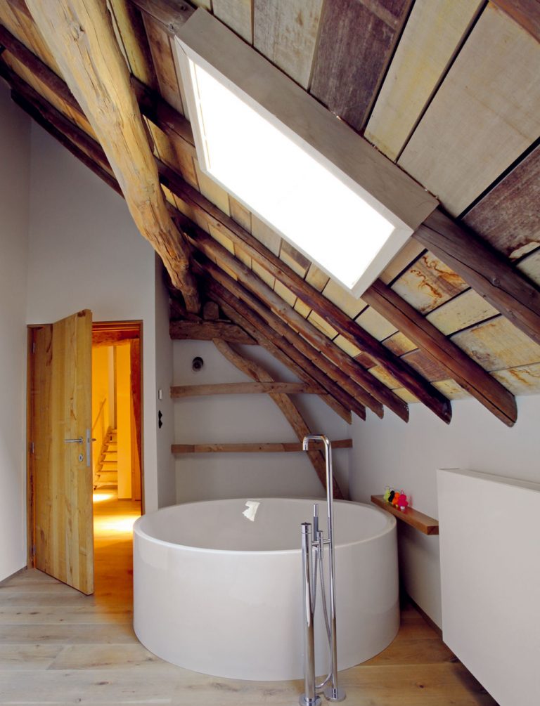 Veľkorysá kúpeľňa je vybavená vaňou, ktorá tvarom pripomína kaďu, atmosféru vidieka potvrdzuje aj odkryté drevo nahrubo opracovaného krovu.