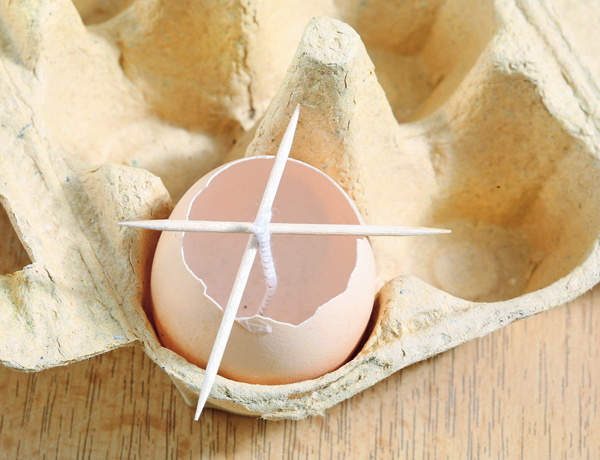 2. Vajíčko rozbite o pohár tak, aby vám zostali 2/3 z pôvodnej veľkosti vajíčka celé. Blanu zvnútra vyberte a do škrupinky vložte pliešok s knôtom. Aby knôt stál rovno, zafixujte ho jedným alebo dvomi špáradlami. 