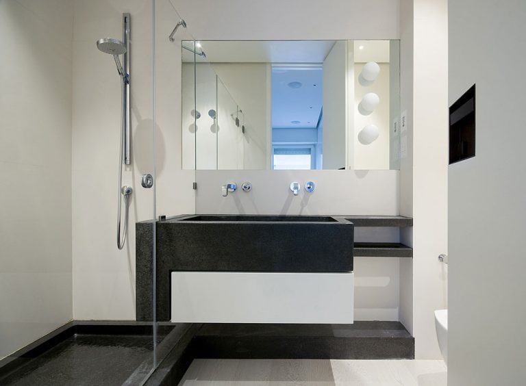 Druhá kúpeľňa pri hlavnej spálni v jednoduchých tvaroch s využitím kontrastu bielej na stenách a čierneho mramoru.