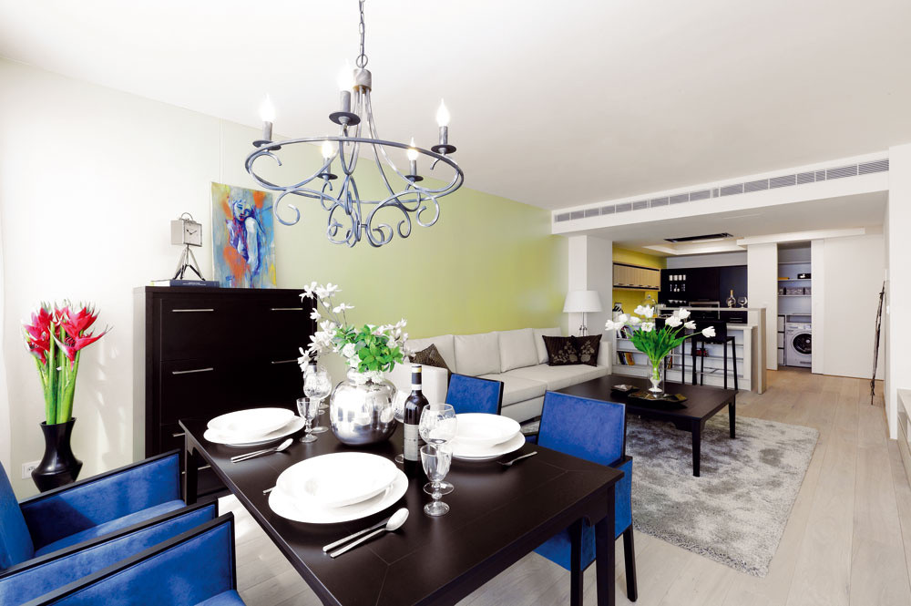 Obývačka je prepojená s kuchyňou a jedálenským kútom pri okne. Jemnú farebnosť a prírodné materiály oživujú atramentové jedálenské stoličky.