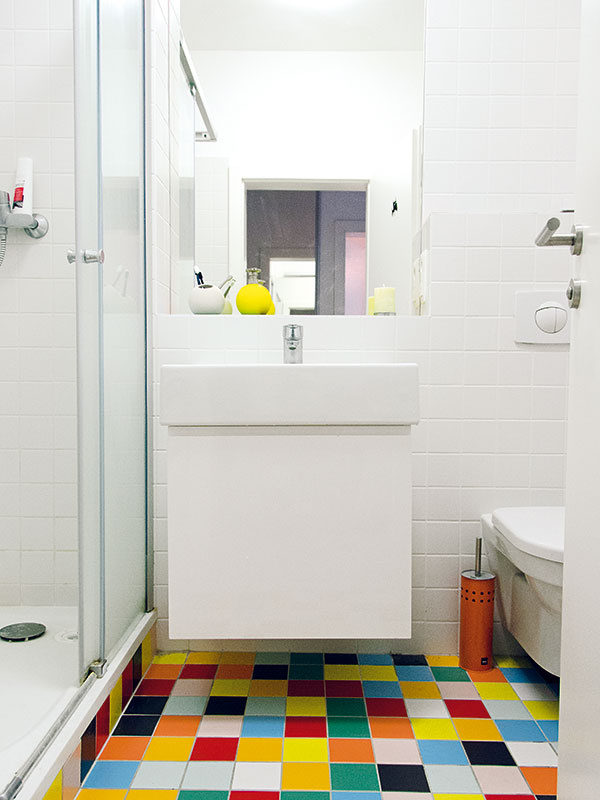 Kúpeľňa je kvôli šetreniu čiastočne vybavená sanitou, ktorú byt dostal „do výbavy“ ešte ako holobyt. Zo stručnej ponuky vybrali architekti a majitelia jednoduché typy, zladili ich s bielou  umývadlovou skrinkou a vhodne nakombinovali s veselou farebnou dlažbou.