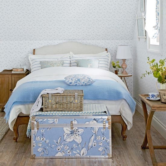 Country style blue floral bedroom, slanting roof, floral wallpaper on walls and ceiling, window with voile blind, floral trim, French style wooden bed with blue and white bedding, floral ottoman, wicker bastet, folding tray table,  IH 05/2013 Pub Orig