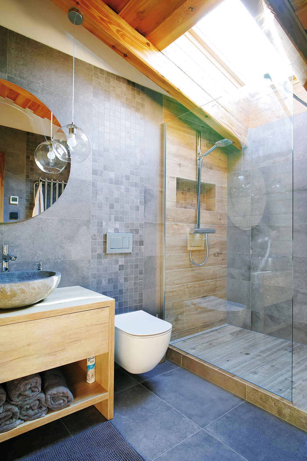PRÍRODNÝ CHARAKTER bol zachovaný aj v kúpeľniach s obkladom, ktorý imituje kameň a drevo. Priehľadné sklo  v sprchovacom kúte a číre svietidlá pocitovo priestor odľahčujú.