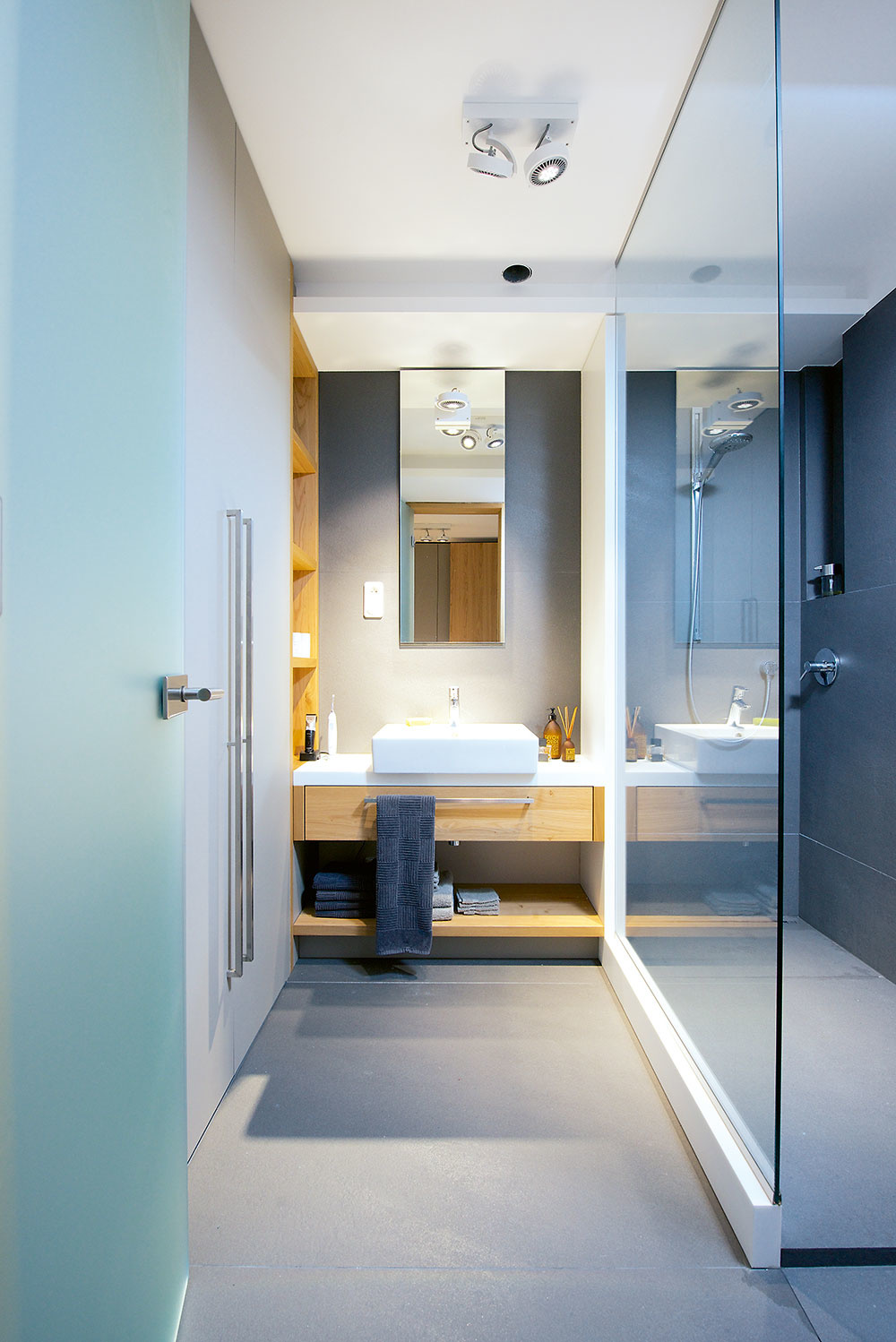 V kúpeľni sa farebné ladenie nemení – kombinácia sivej, dreva a bielej keramiky je elegantná a navodzuje pokojnú atmosféru. Aj tu sú funkčnosť a precíznosť detailov dovedené k dokonalosti.