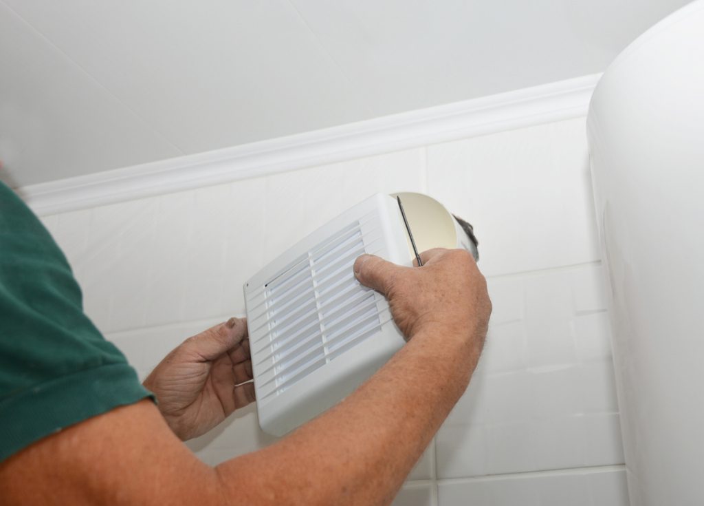 Handyman installing new bath vent fan, ventilation system in the house bathroom . Bath fan repair, installation.