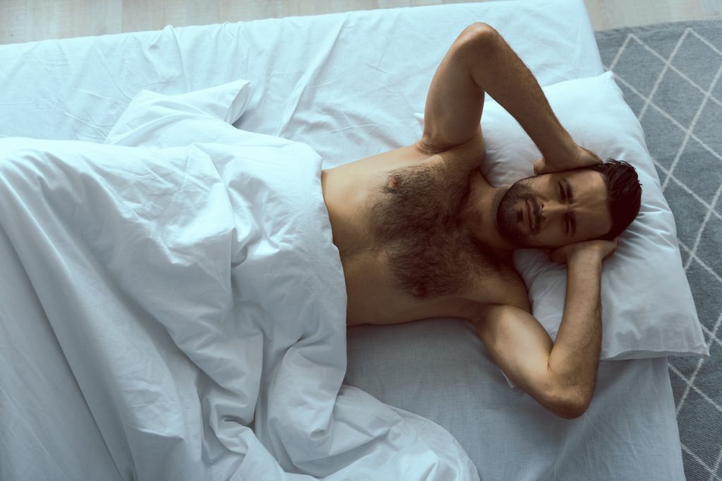 Muž zakrývajúci si uši pred hlukom v posteli