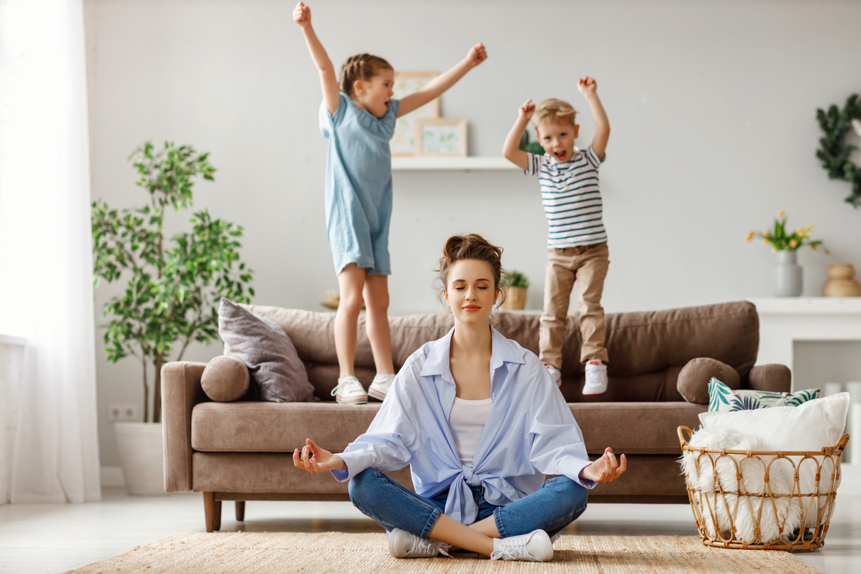 Tranquil young mother practicing yoga to stay calm with mischievous kids at home