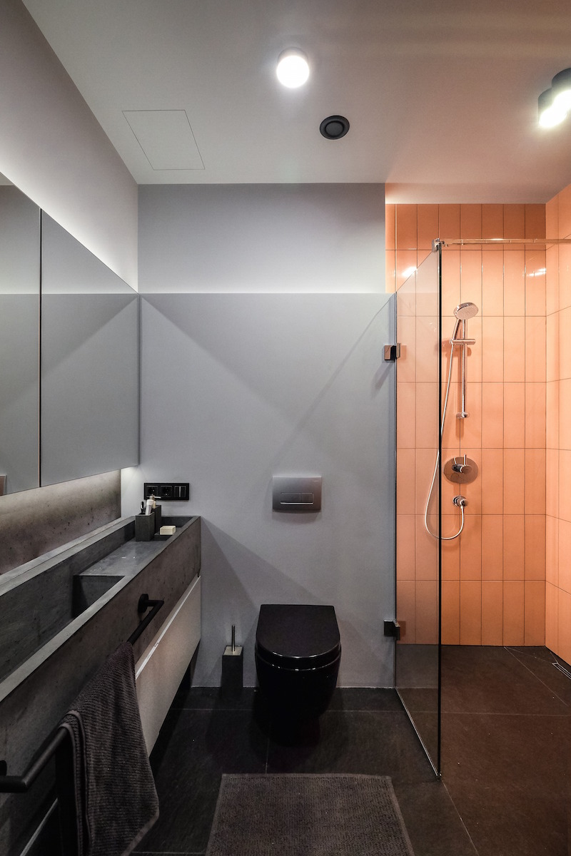 Minimalistickú kúpeľňu poňali architekti podobne ako zvyšok bytu. Sivo-čiernu farebnú kombináciu a betón „rozbili“ nápadnými oranžovými kachličkami.
