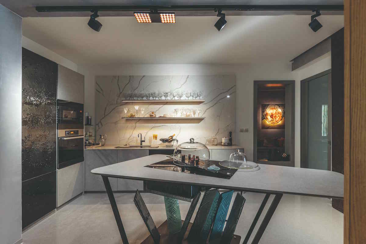 Kuchyňa s ostrovom pôsobí elegantným dojmom vďaka striedmej sivo-čiernej farebnosti a nádych luxusu jej dodáva mramorový obklad či sklenené obloženie dvierok umývačky a chladničky v podmanivej čiernej. Gordanine návrhy pretavuje do reality TechniStone. Autorka vyzdvihuje spojenie kameňa a skla, ktoré tkvie v krehkosti a sile. 