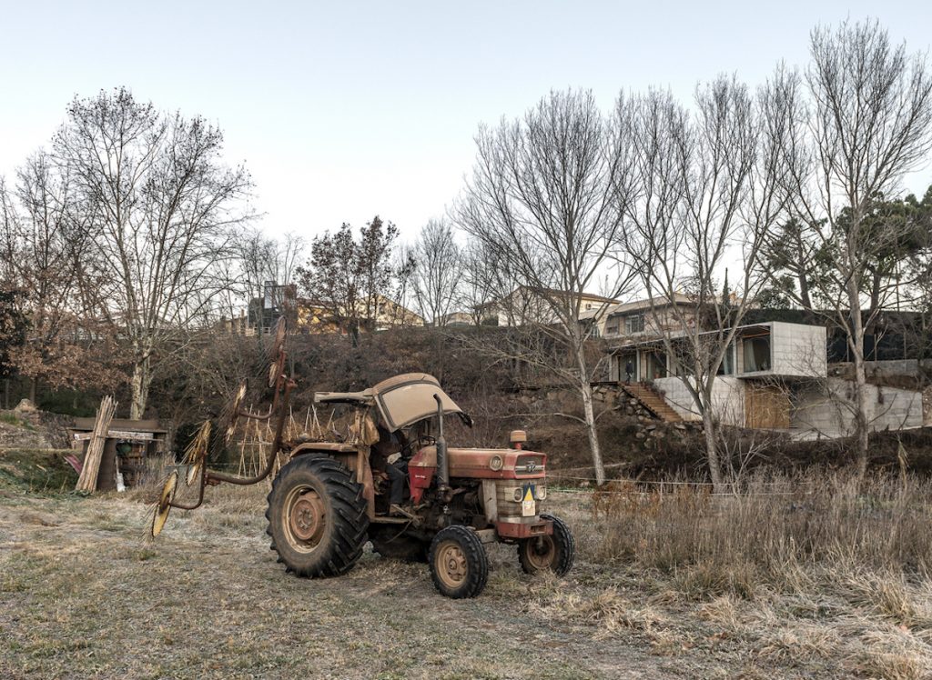 Traktor na pozemku v pozadí hranatý rodinný dom