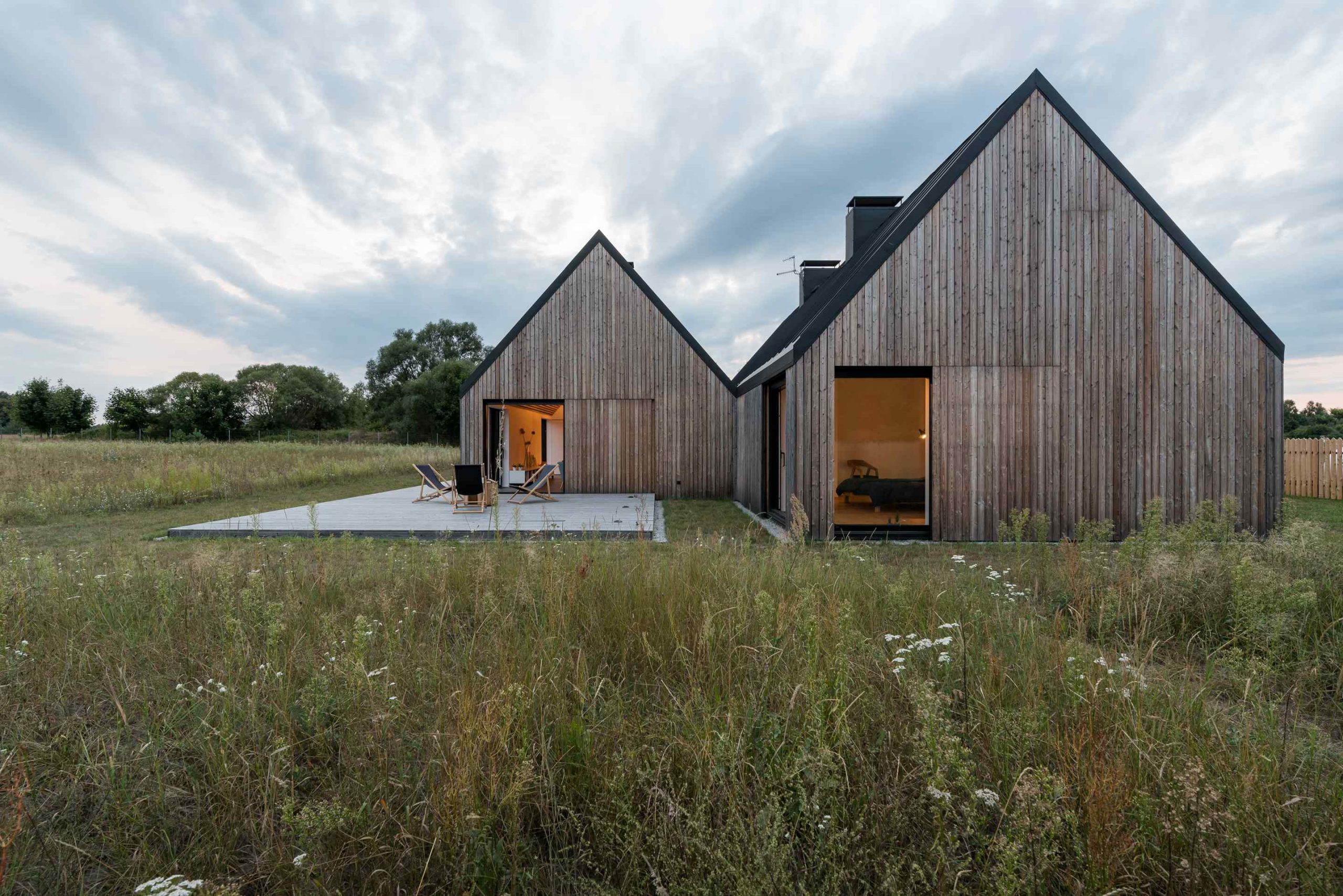 Dva rovnaké drevené domy na lúke s terasou