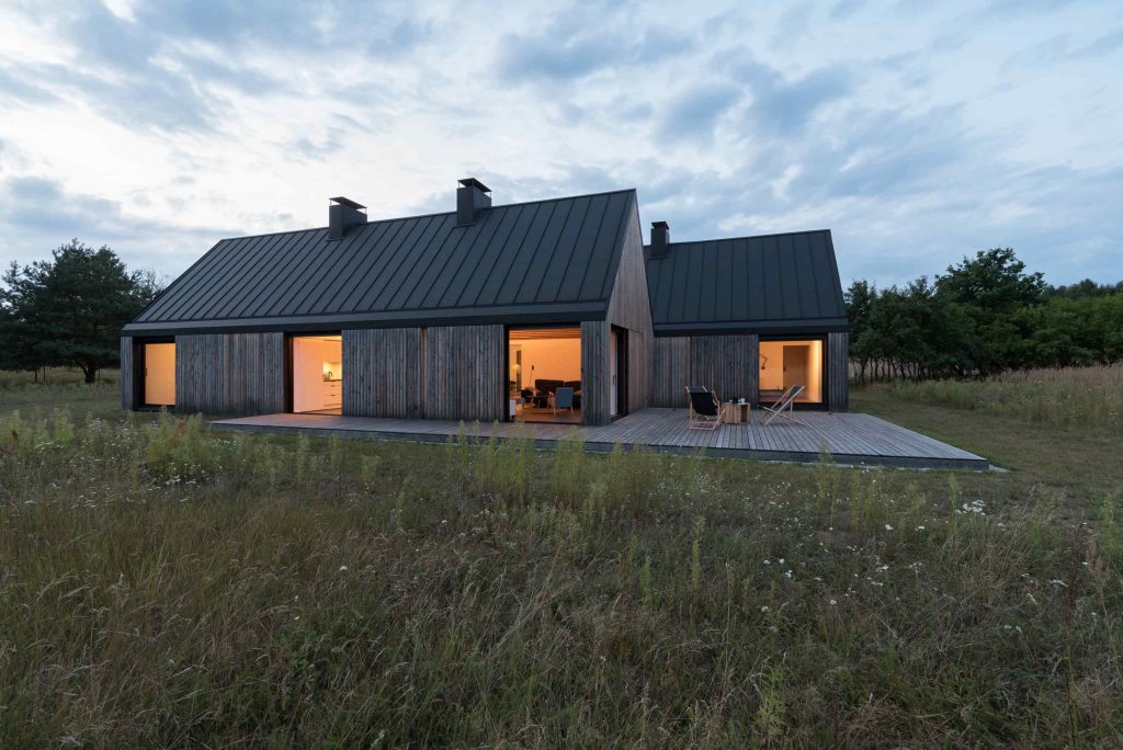Dva rovnaké drevené domy na lúke s terasou