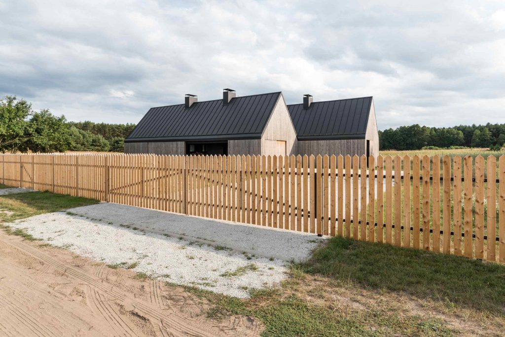 Dva rovnaké drevené domy na lúke s tradičným plotom