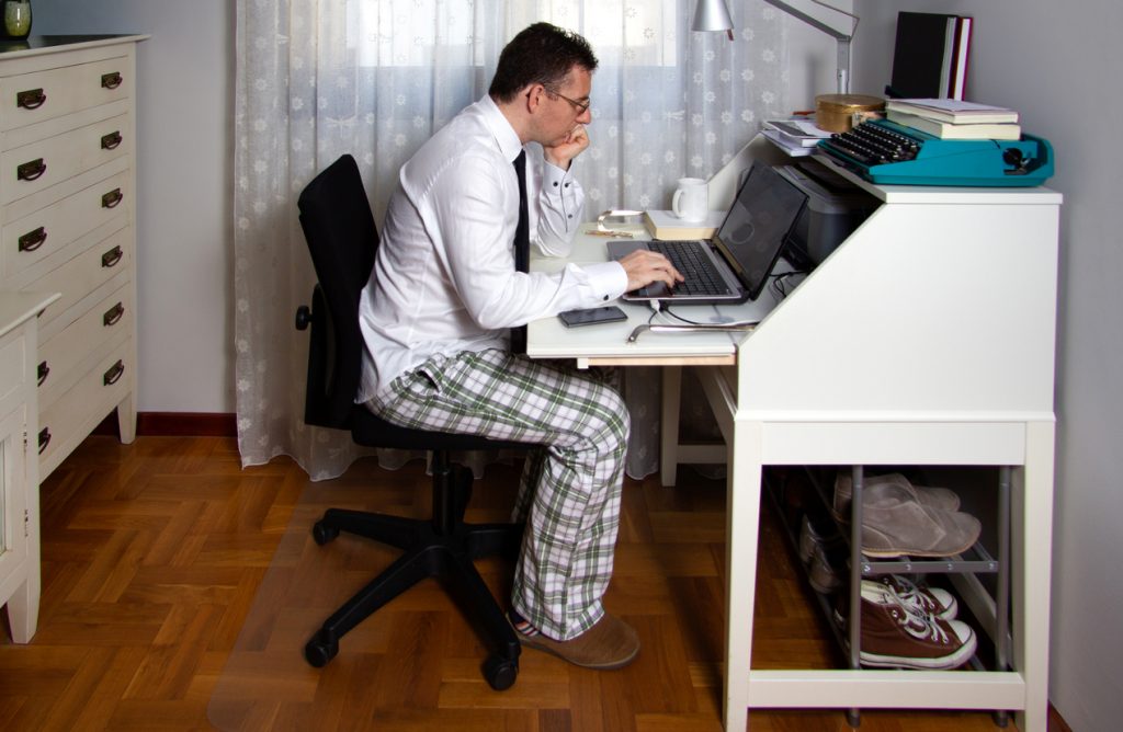 Muž za pracovným stolom doma v pyťžamových nohaviciach
