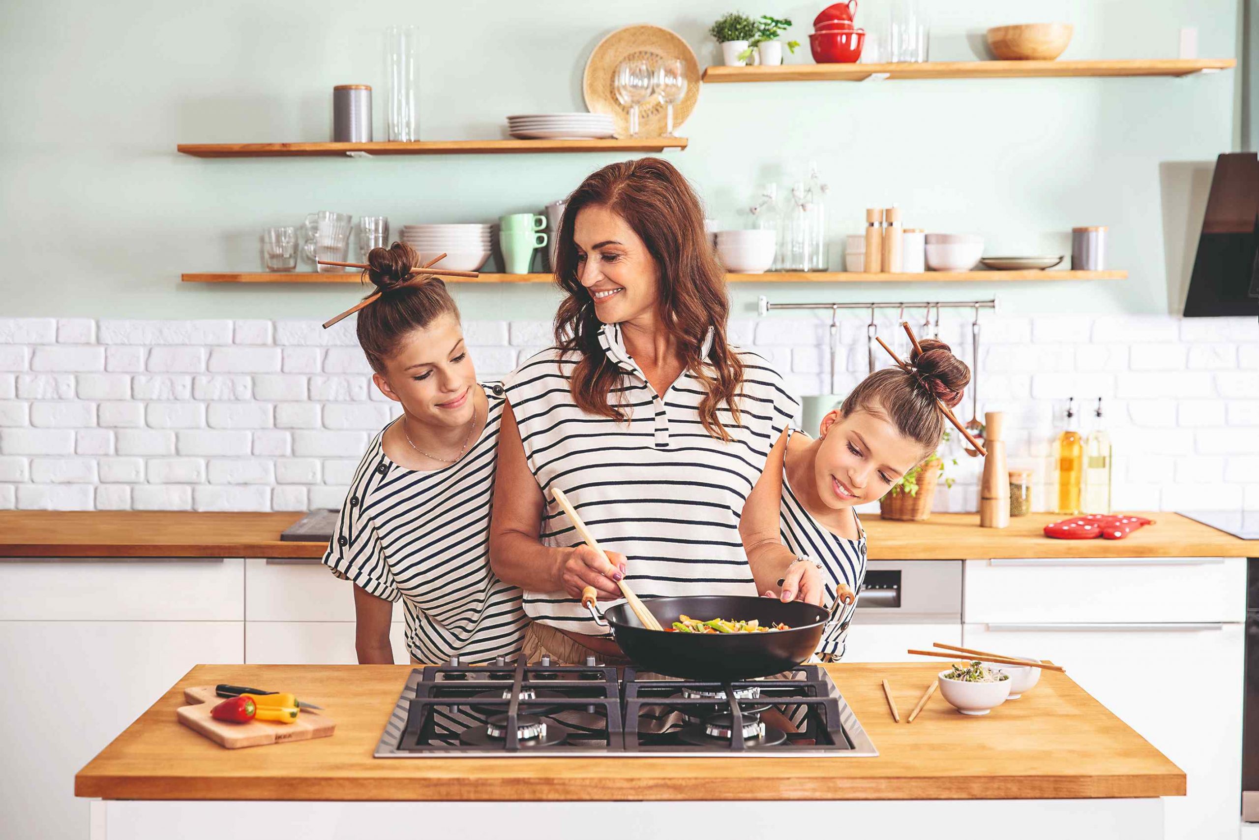 Žena varí v kuchyni s dvoma dcérami a rovnakých tričkách