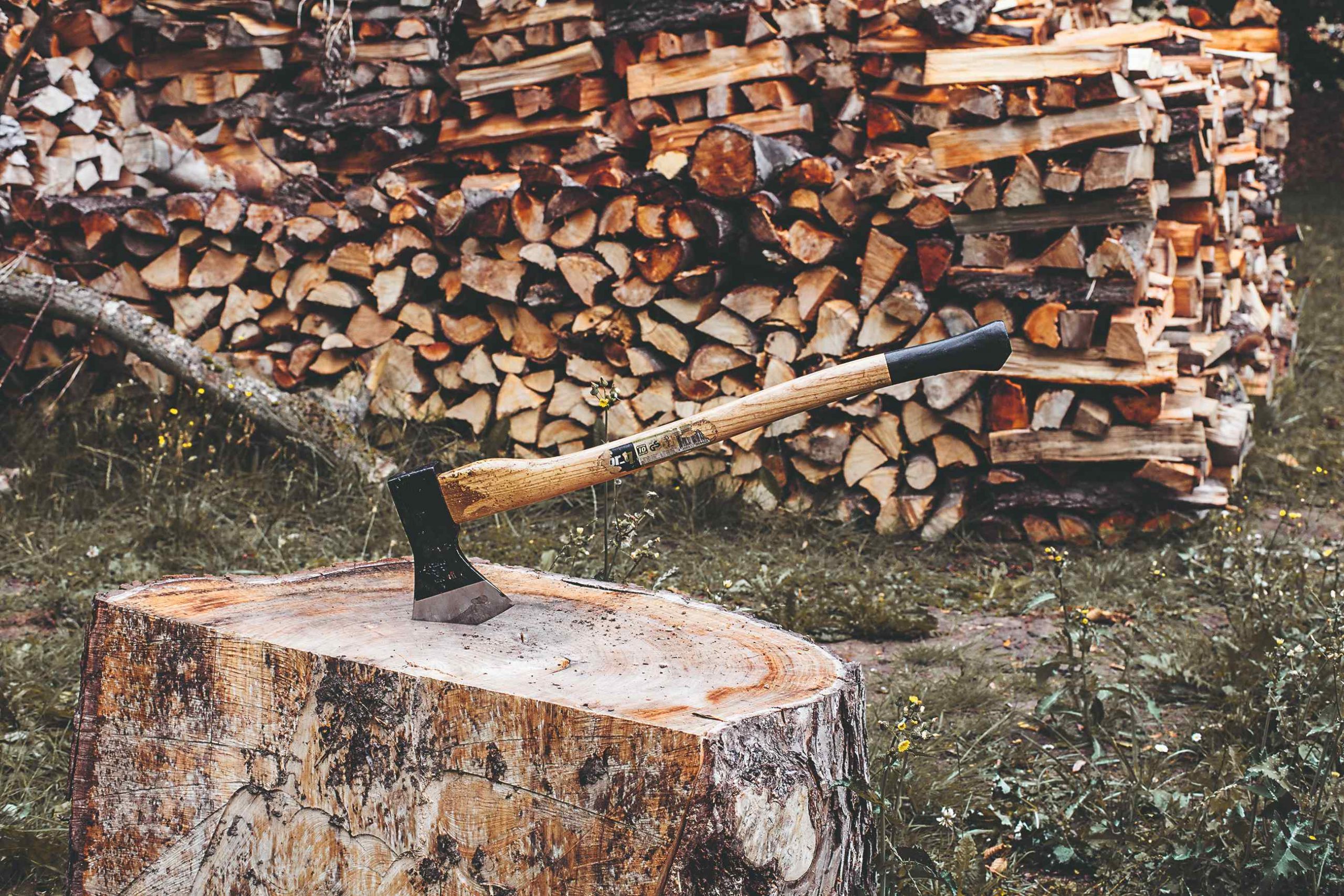 Sekera zaťatá v pni pred naskladaným drevom