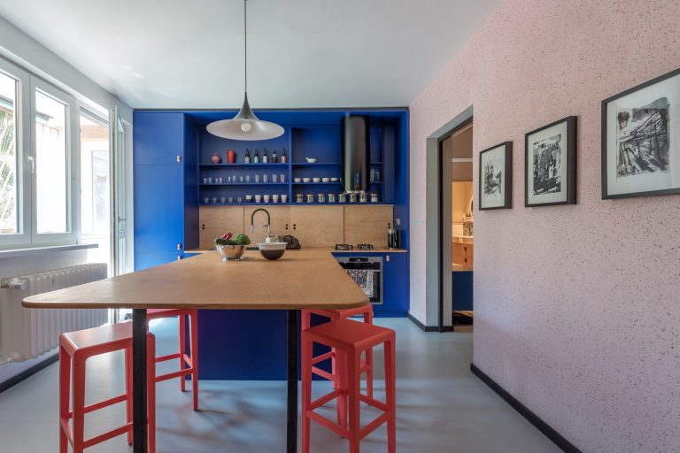 Výrazná modrá kuchyňa so svetlým drevom a červenými stoličkami