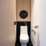 Úzka toaleta s čiernou podlahou a drevenou skrinkou