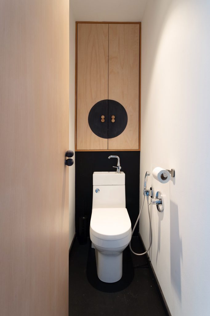 Úzka toaleta s čiernou podlahou a drevenou skrinkou