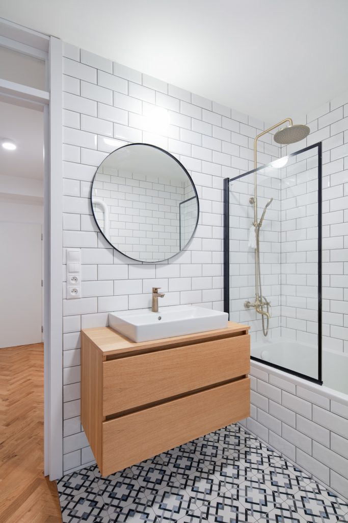 Biela kúpeľňa s mozajkovou dlažbou a okrúhlym zrkadlom