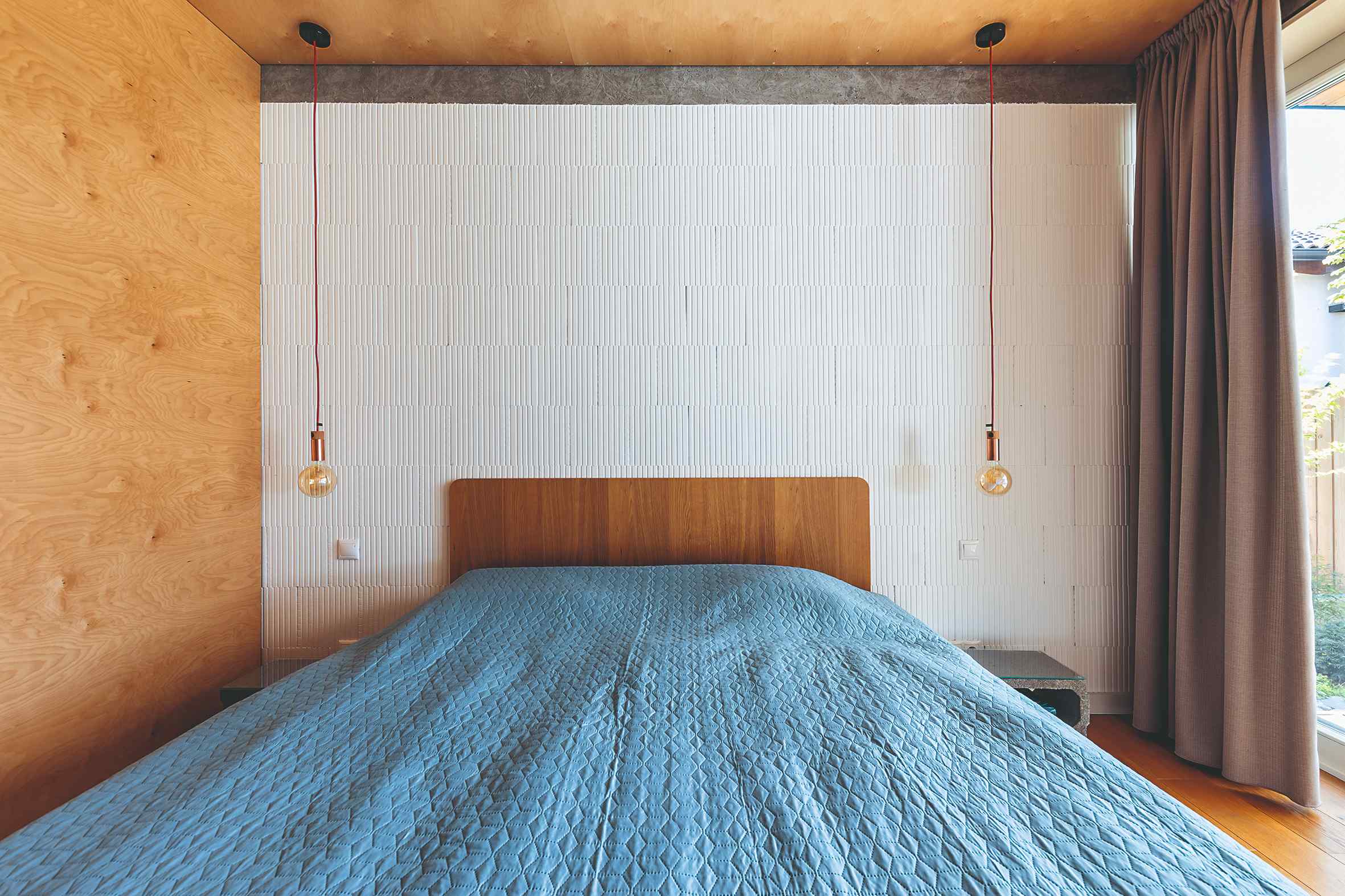 Spálňa s preglejkou na stene posteľ s modrým prehozom