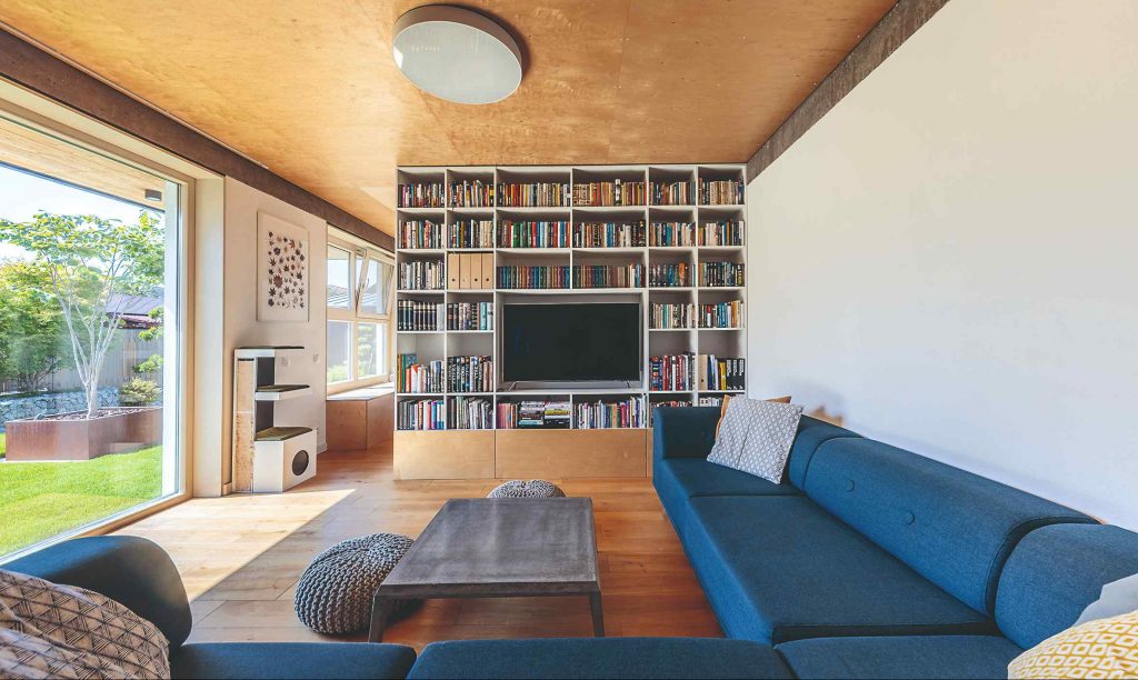 Obývačka s preglejkovým stropom modrým gaučom a veľkým presklením