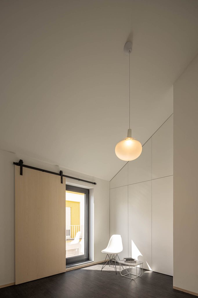 Biela minimalistická miestnosť so šikmou stenou a zasúvacími dverami