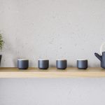 Čierne šálky na čaj s čajníkom na drevenej poličke