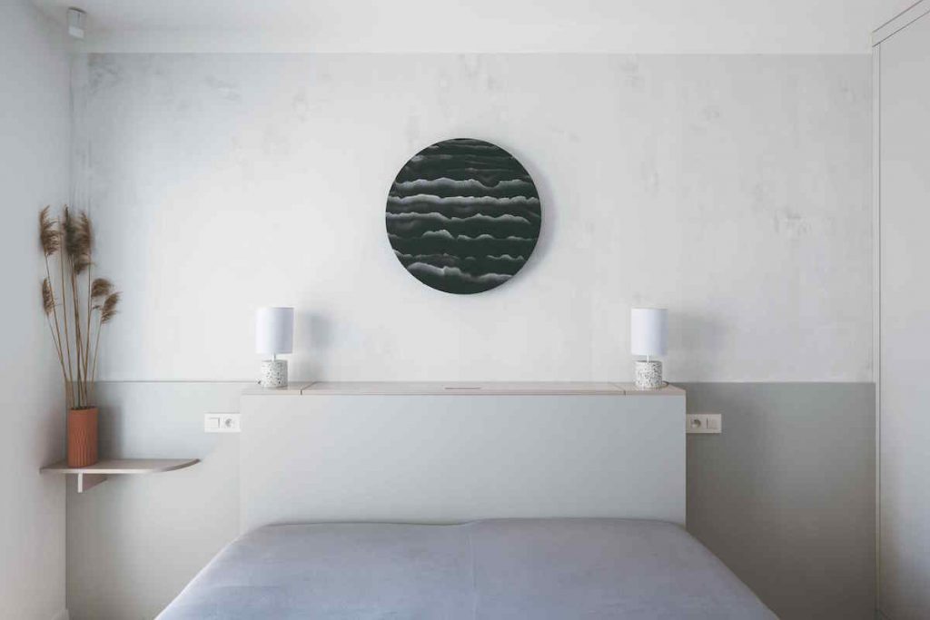 Jednoduchá sivá spálňa s kruhovým obrazom nad posteľou
