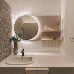 Biela malá kúpeľňa s okrúhlym zrkadlom a terrazzo stenou