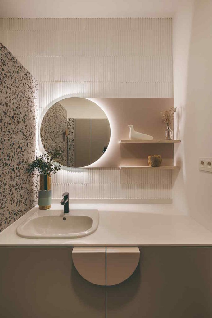 Biela malá kúpeľňa s okrúhlym zrkadlom a terrazzo stenou