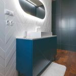 Biela kúpeľňa s modrou skrinkou a oválnym zrkadlom