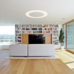 Presklená obývačka s veľkou knižnicou a bledým gaučom