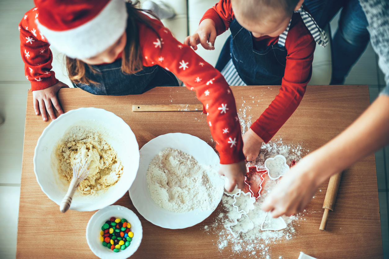 Upper view photo of children making cookies using flour and dough for christmas wearing santa clothes