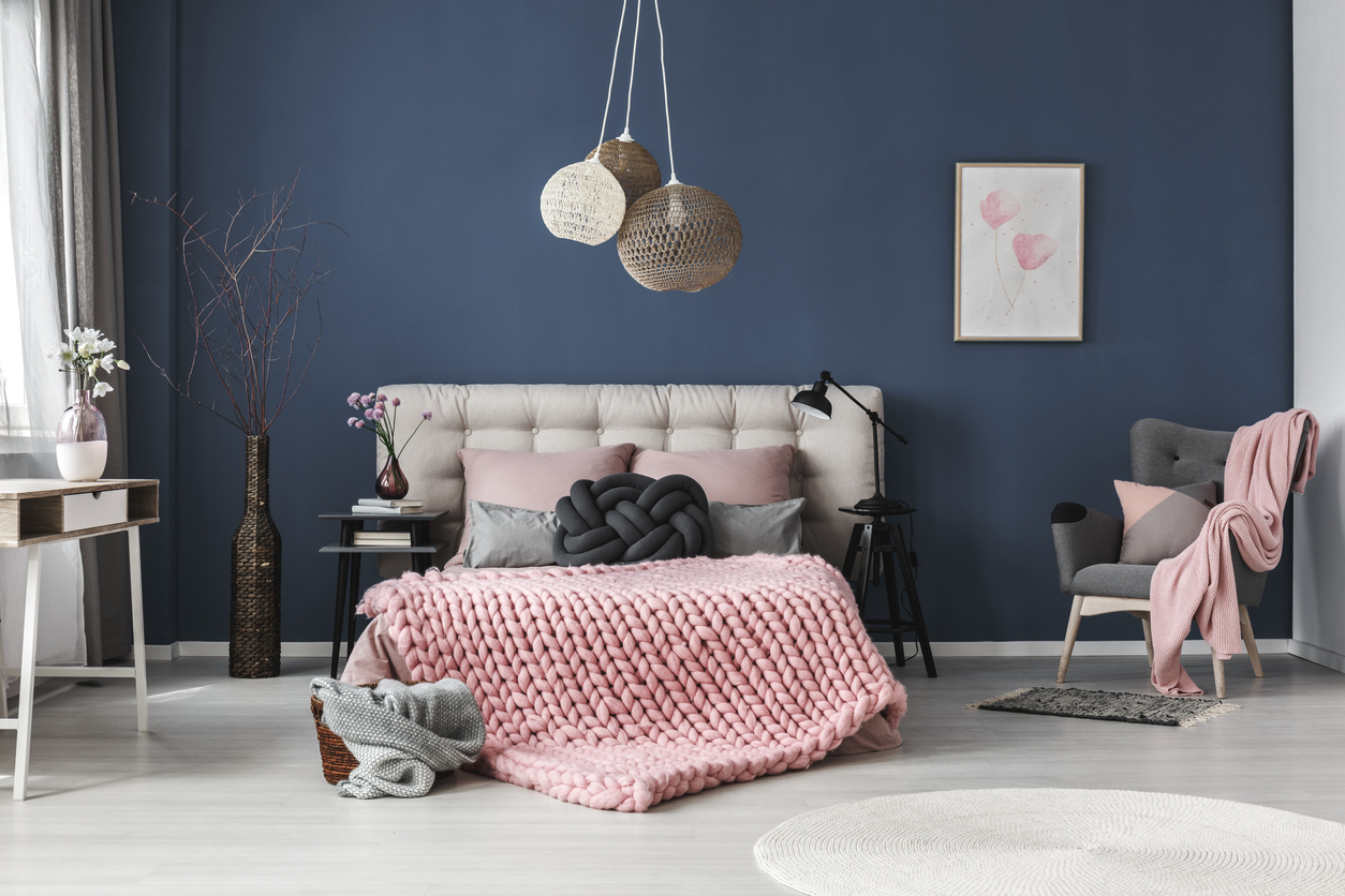 Spálňa s modrou stenou čalúnenou posteľou a vlnenou ružovou dekou