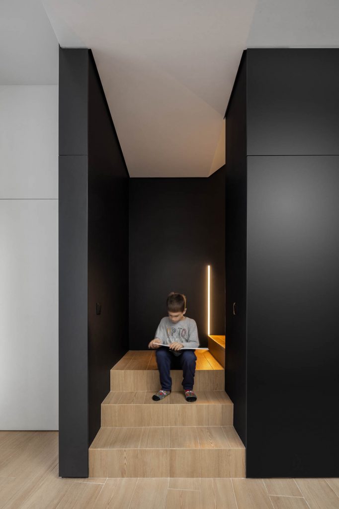 Sediaci chlapec na schodisku zo svetlého dreva s čiernymi stenami