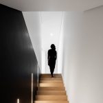 Žena na schodisku zo svetlého dreva s čiernymi stenami