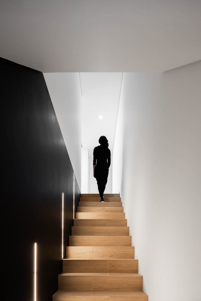 Žena na schodisku zo svetlého dreva s čiernymi stenami