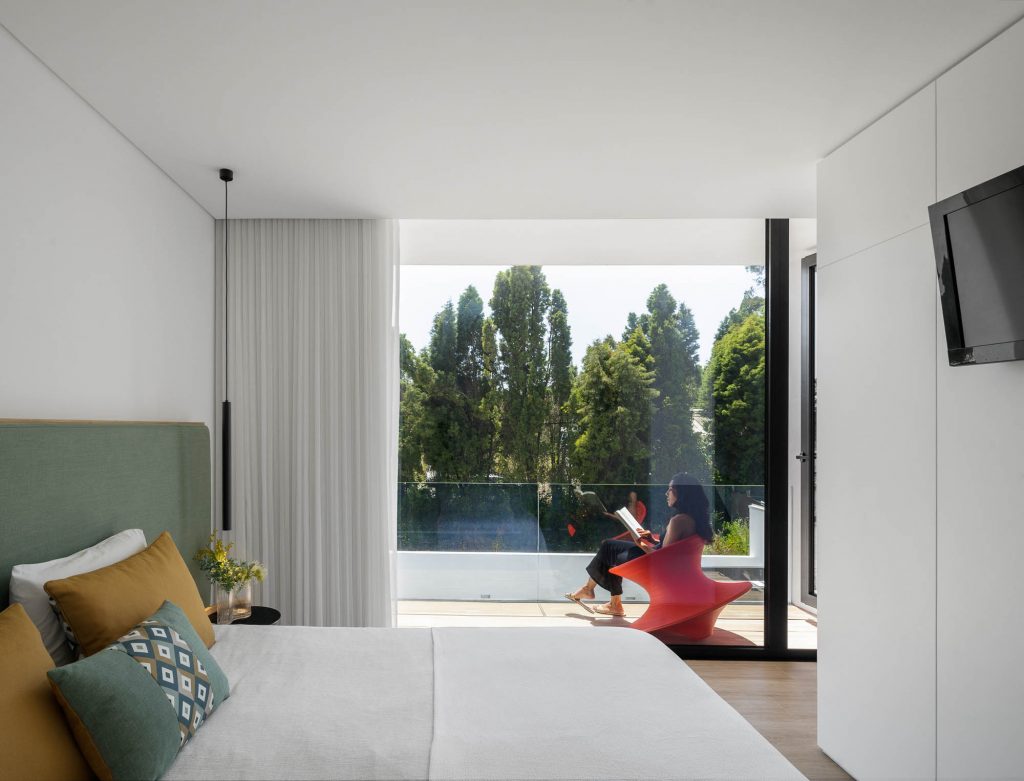 Moderná spálňa s presklenou terasou a ženou sediacou na dizajnovom kresle