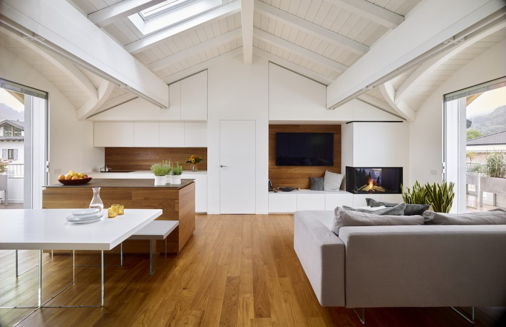 Strešný byt s bielym dreveným krovom a hnedým nábytkom a šedou sedačkou