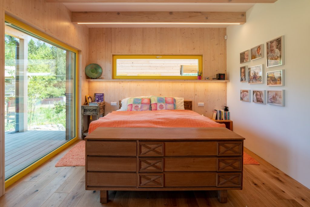 Prírodná spálňa s drevenou komodou a oranžovým prehozom