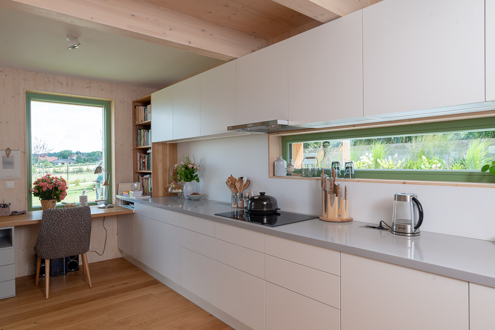 Biela kuchyňa s drevenou podlahou a zelenými oknami