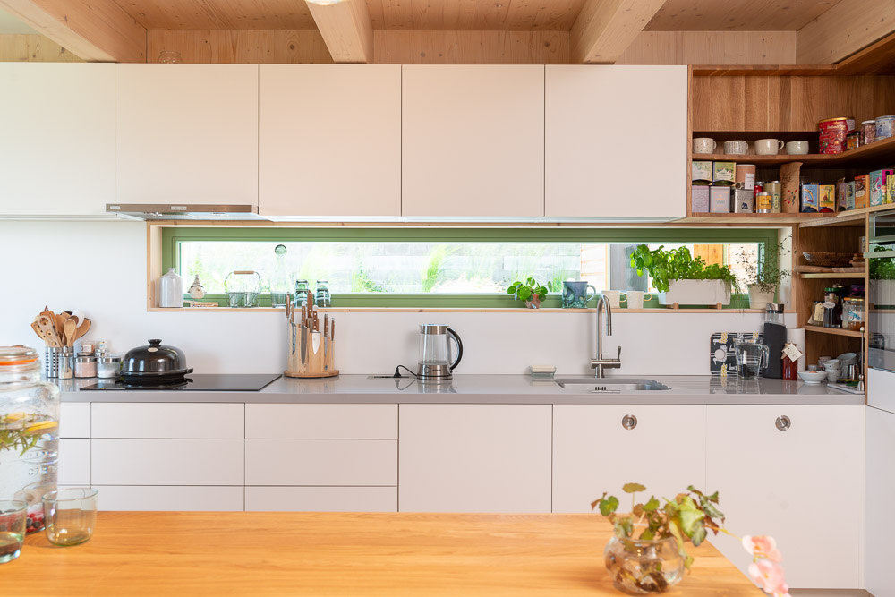 Biela kuchyňa s drevenou podlahou a zelenými oknami