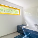 Biela kúpeľňa s modrými kachličkami a žltým rámom okna
