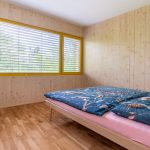 Jednoduchá spálňa v drevostavbe s veľkým pozdĺžnym oknom