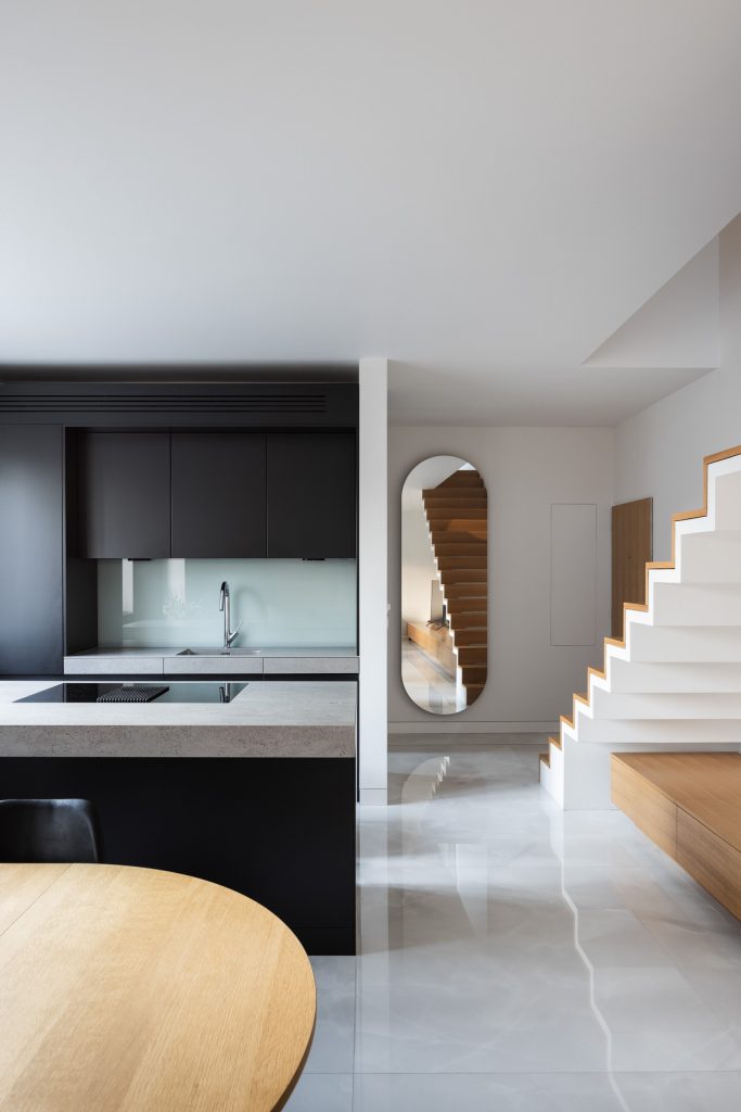 Moderná svetlá obývačka so schodiskom a čiernou kuchyňou
